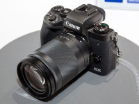 Een Canon 'mirrorless' camera met een gemonteerde lens, op de lens is de ronde witte stip zichtbaar / Bron: Morio, Wikimedia Commons (CC BY-SA-3.0)