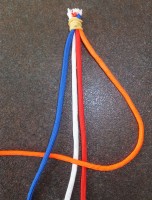 Kruis de oranje werkdraad over de rode en witte leidraden heen en vervolgens onder de blauwe werkdraad door. Trek de zo ontstane knoop aan.