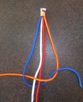 Kruis de blauwe draad onder de witte en rode draad door en over de oranje draad en trek ook deze knoop aan.